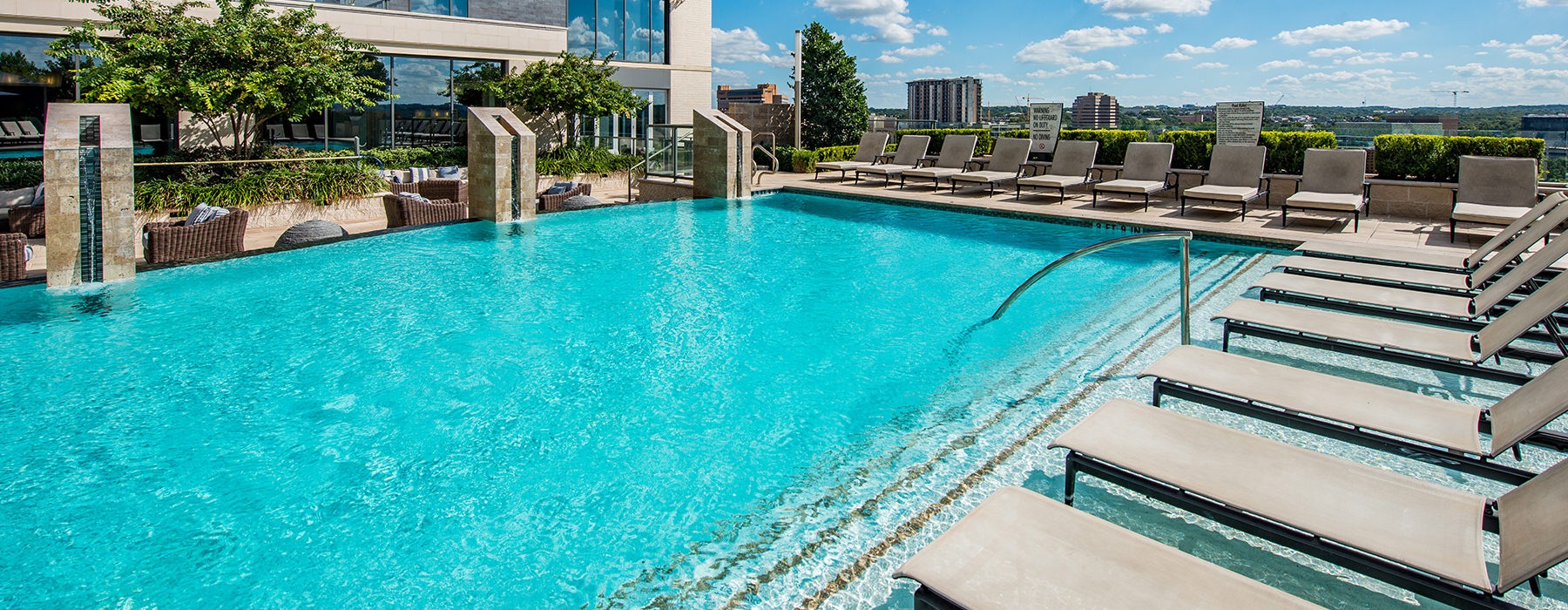 Large resort style sparkling blue swimming pool surrounded by a massive deck with plenty of seating.